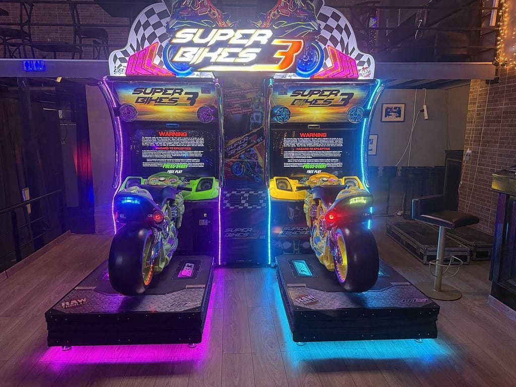 Δύο αγωνιστικά μηχανήματα μοτοσικλέτας arcade στημένα δίπλα δίπλα σε εταιρική εκδήλωση