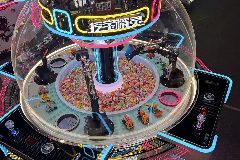 Στρογγυλό crane machine (γερανάκι δώρων) με διάφανο θόλο και ρομποτικούς βραχίονες, γεμάτο καραμέλες και μικρά δώρα, στην GTI China Expo 2026