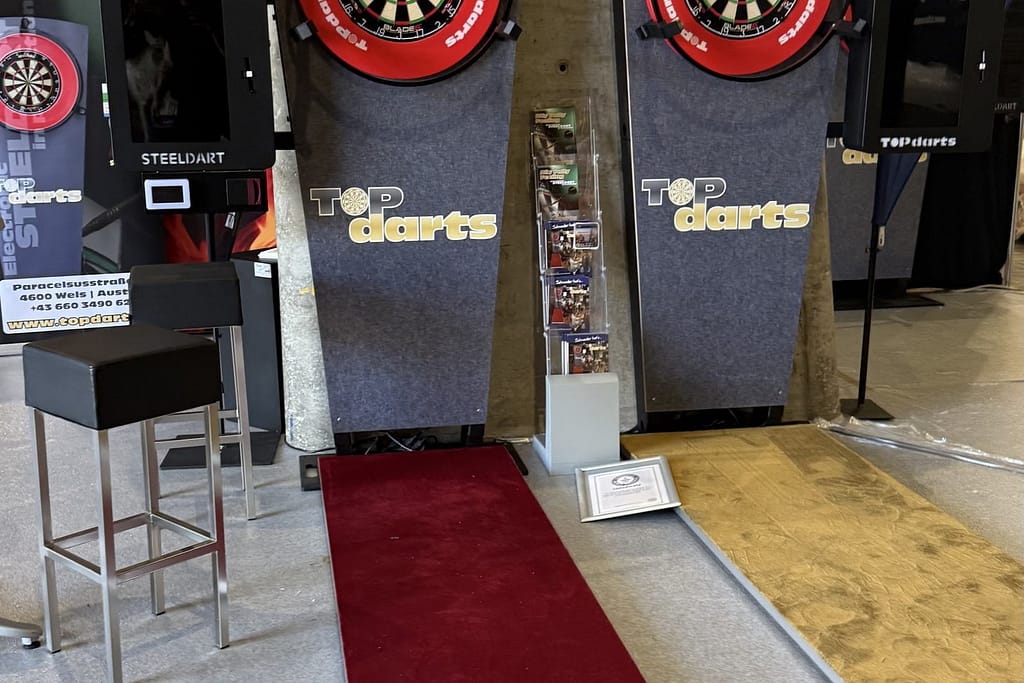 Μηχανήματα ηλεκτρονικών βελακιών darts με κόκκινο χαλί, σε περίπτερο της IAAPA Expo Europe 2025