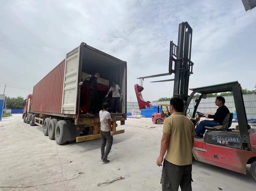 Αυλή φόρτωσης με ανοιχτό container, κλαρκ και γερανό που σηκώνει κόκκινο μεταλλικό βραχίονα