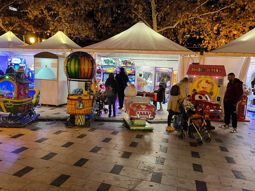Kiddie rides και κερματοφόρα μηχανήματα μπροστά από λευκές τέντες στην πλατεία Αριστοτέλους