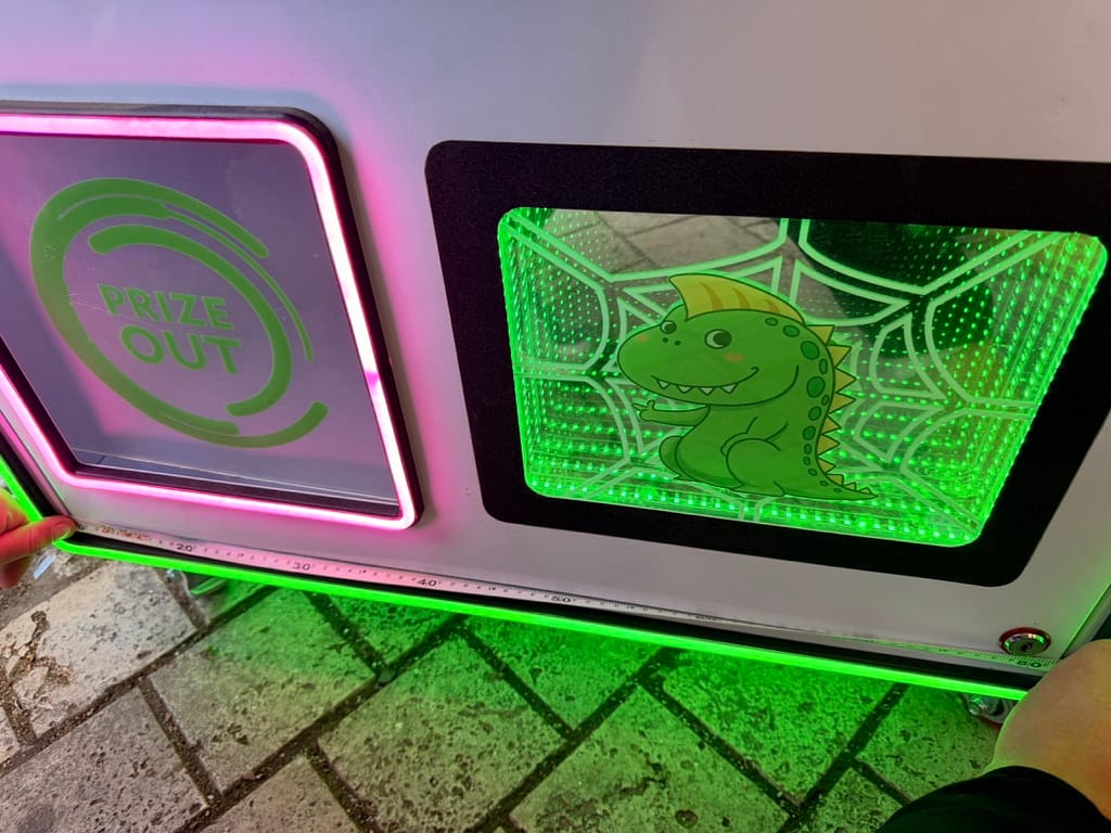 Θυρίδα επάθλων με ροζ neon και φωτιστικό πάνελ με το πράσινο δεινοσαυράκι
