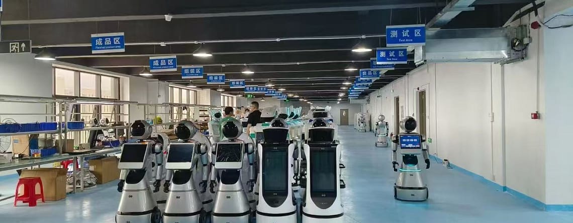 Αίθουσα παραγωγής εργοστασίου με σειρές από λευκά ρομπότ υπηρεσίας, γαλάζιο δάπεδο και μπλε πινακίδες ζωνών κρεμασμένες από την οροφή