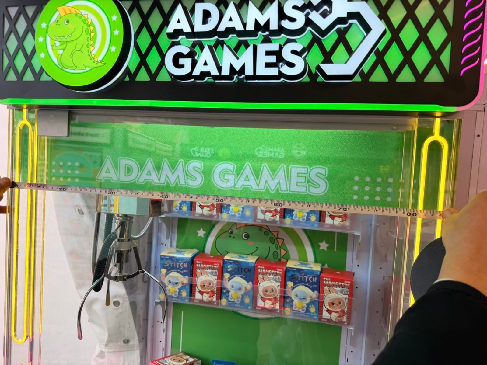 Γερανός AdamsGames με φωτιζόμενη πινακίδα, αρπάγη και έπαθλα πίσω από το τζάμι