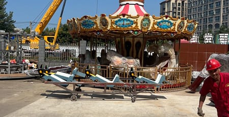 Καρουζέλ υπό συναρμολόγηση στον αύλειο χώρο εργοστασίου, με κινητό γερανό δίπλα
