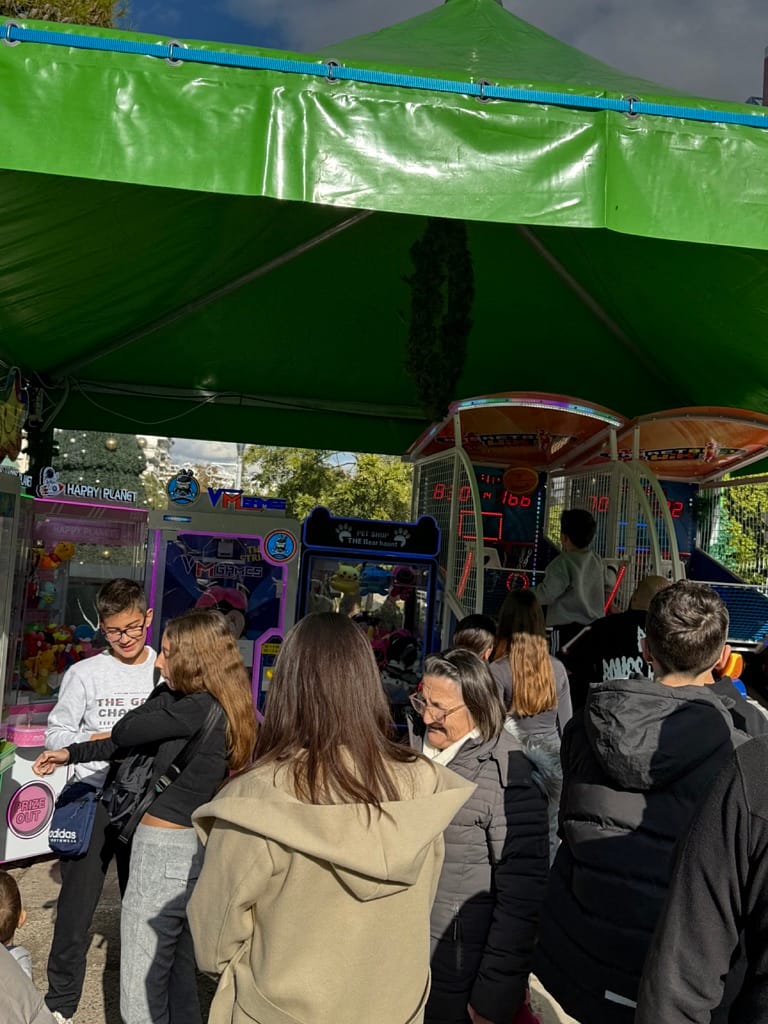 Κόσμος μέσα στο περίπτερο, γερανάκια με λούτρινα και μπασκέτες arcade με φωτεινό ταμπλό