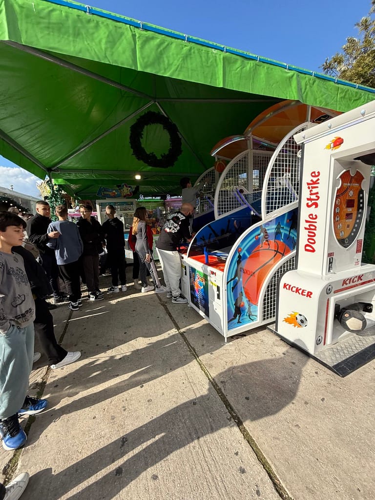 Έφηβοι περιμένουν σειρά στις μπασκέτες arcade κάτω από πράσινη τέντα σε πλατεία